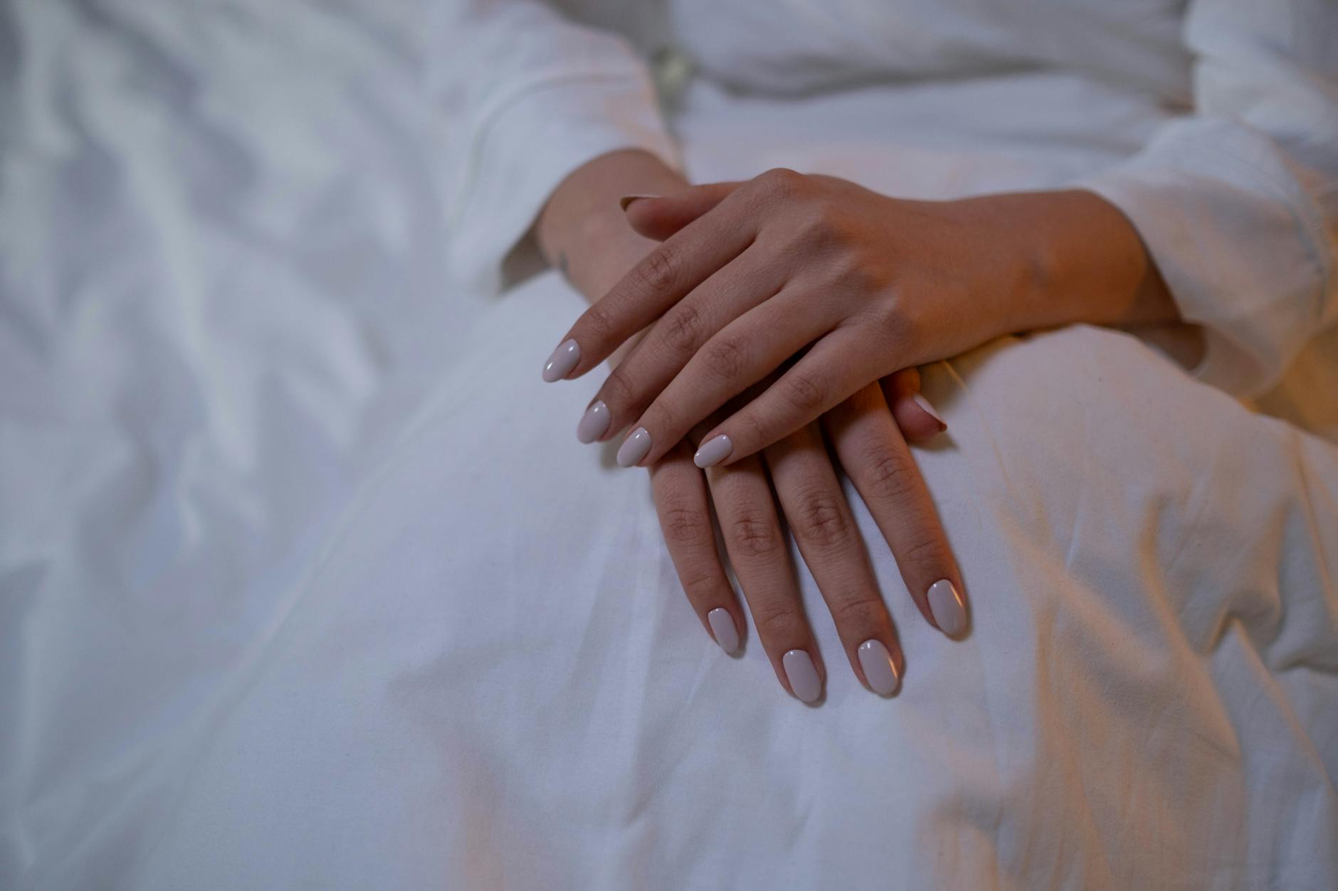 Dłonie z minimalistycznym, nude manicure spoczywające na białej tkaninie