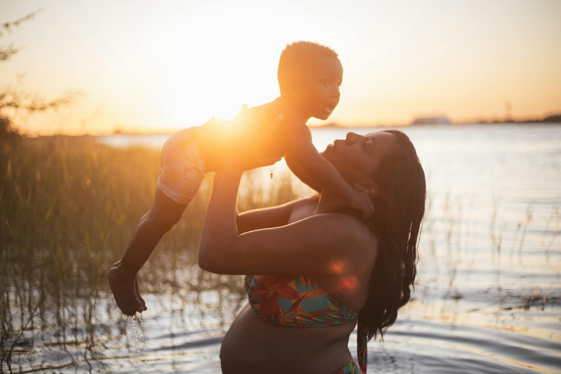 Mama podnosi dziecko na plaży o zachodzie słońca