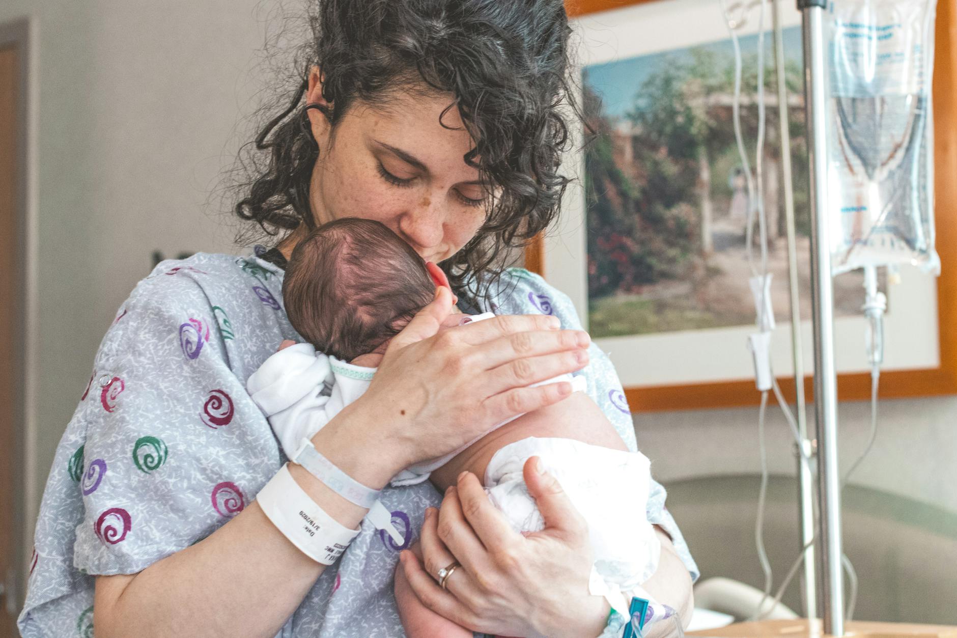 Mama tuląca noworodka na szpitalnym łóżku po porodzie