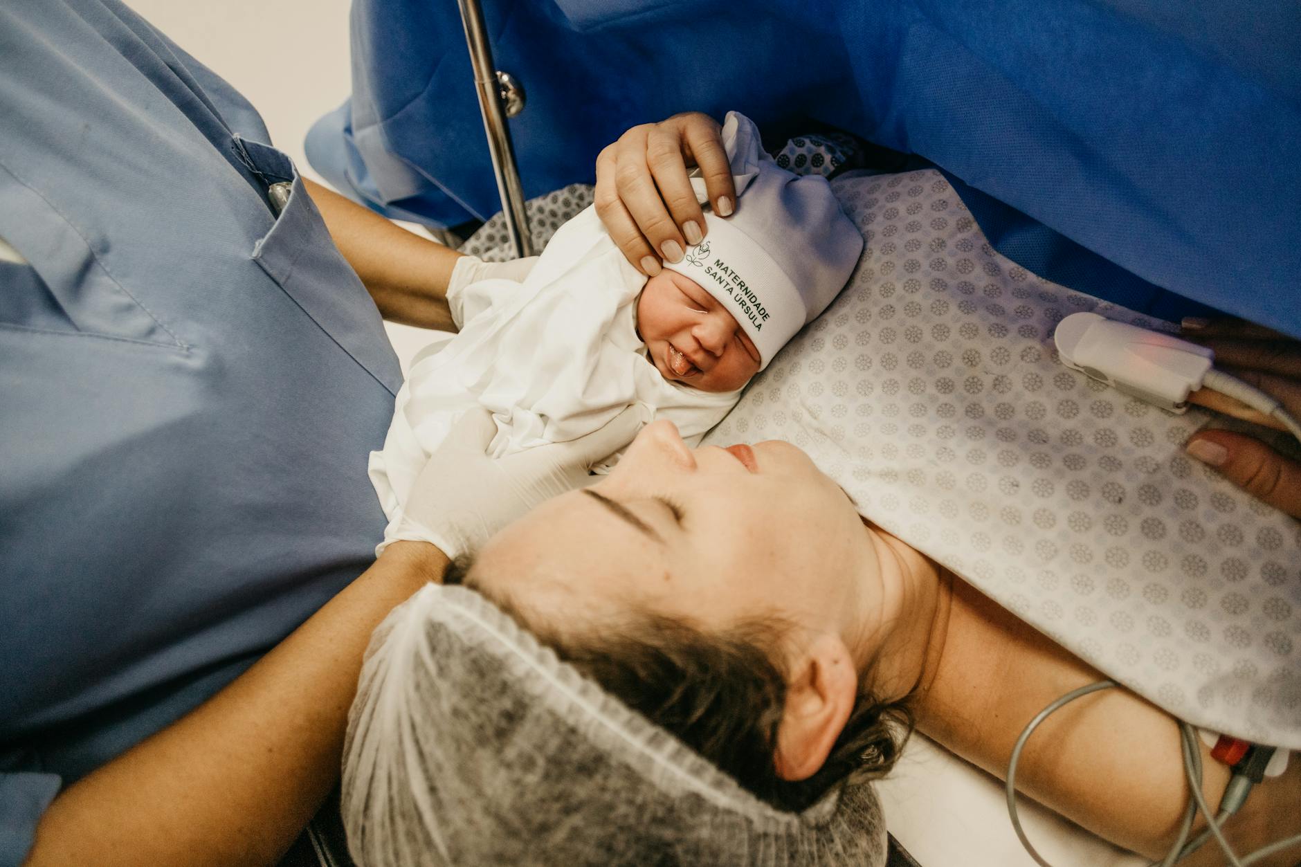 Mama tuląca noworodka na szpitalnym łóżku tuż po porodzie