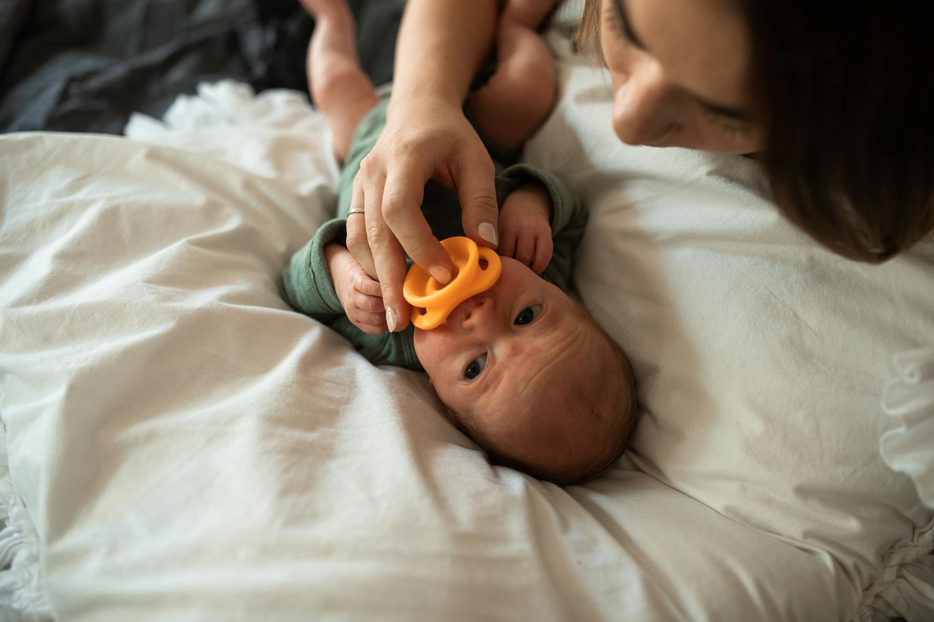 Mama tuląca noworodka w domu, trzymając w dłoni smoczek