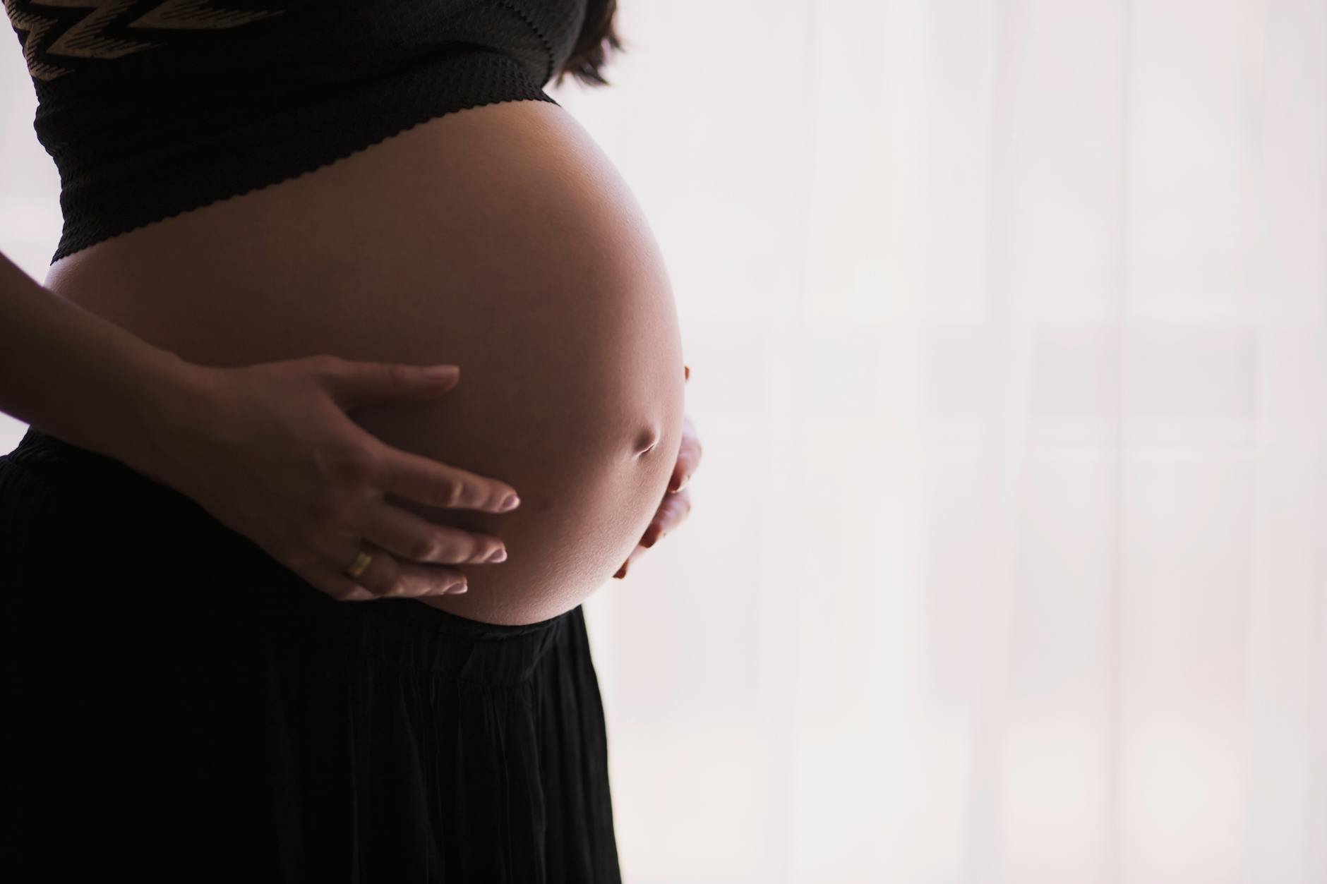 Zbliżenie na ciężarną kobietę delikatnie trzymającą nagi brzuch