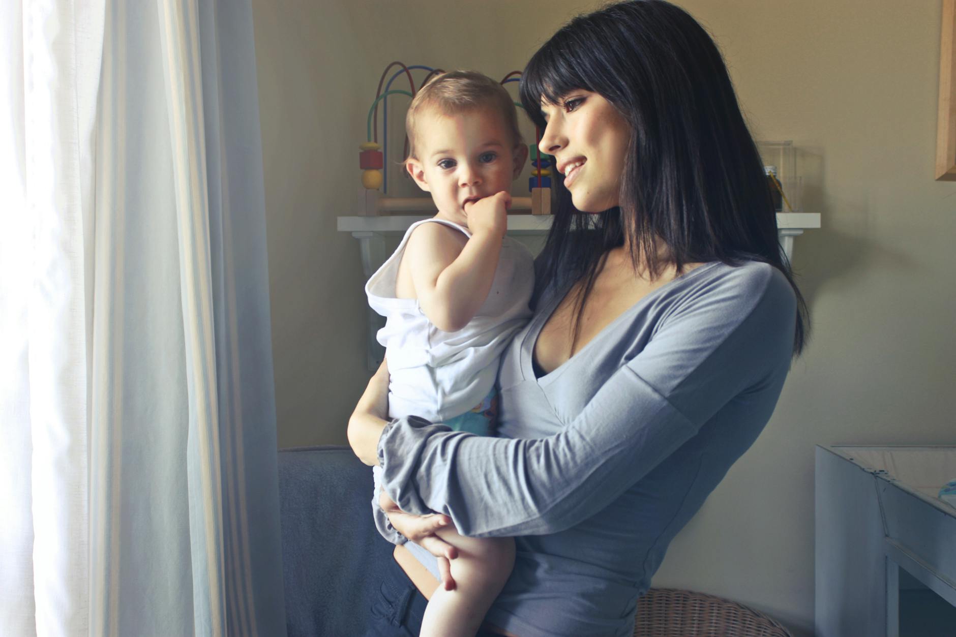 Mama przytula niemowlę przy oknie w ciepłym, miękkim świetle