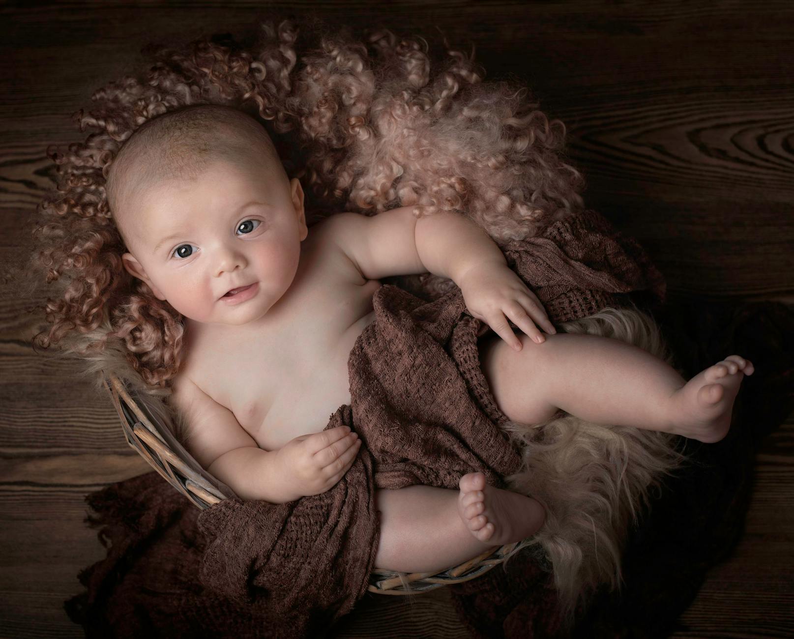 Niemowlę w wiklinowym koszu na brązowym kocu w studiu fotograficznym