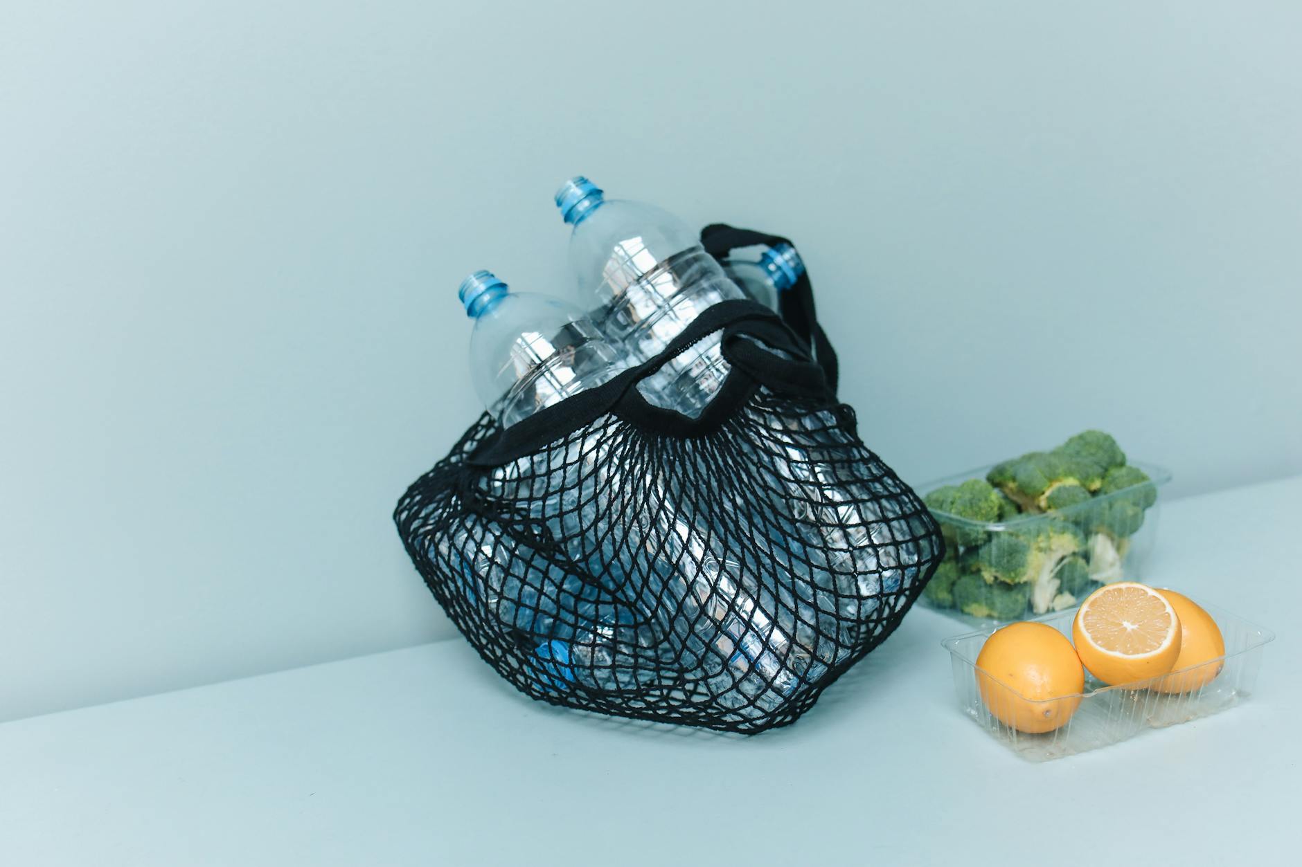 Siatka z butelkami plastikowymi, brokułem i cytrynami jako symbol zero waste